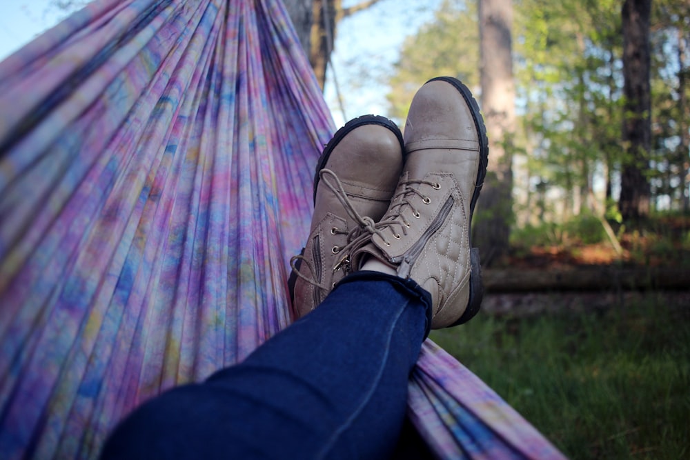 person lying on pink and purple hammock surrounded with trees