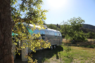 Close-up of a sleek HF trailer parked by a lake, reflecting the vibrant blue sky and surrounding nature.