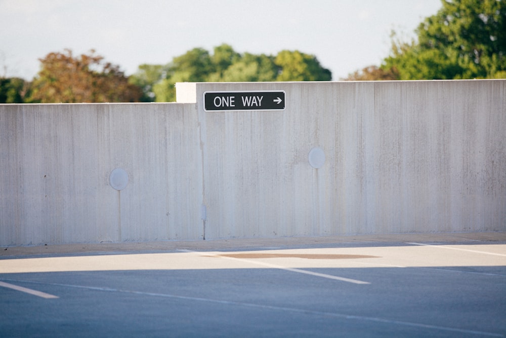 black and white one way signage on gray concrete wall