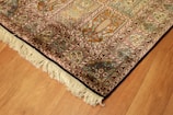 A richly detailed ornate Persian rug with intricate patterns in shades of orange, blue, and cream. The design includes floral motifs and geometric shapes, bordered with a fringe on one edge. Positioned on a wooden floor, the rug showcases traditional craftsmanship.