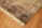 A richly detailed ornate Persian rug with intricate patterns in shades of orange, blue, and cream. The design includes floral motifs and geometric shapes, bordered with a fringe on one edge. Positioned on a wooden floor, the rug showcases traditional craftsmanship.