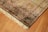 A richly detailed ornate Persian rug with intricate patterns in shades of orange, blue, and cream. The design includes floral motifs and geometric shapes, bordered with a fringe on one edge. Positioned on a wooden floor, the rug showcases traditional craftsmanship.