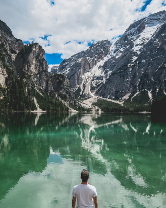 man standing in front of lake and cliff under white clouds and blue sky in Parco naturale di Fanes-Sennes-Braies Italy