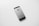 A black and silver smartphone, likely an older model iPhone, is placed on a plain white surface. The device is photographed from the back side, displaying the Apple logo prominently in the center.