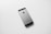 A black and silver smartphone, likely an older model iPhone, is placed on a plain white surface. The device is photographed from the back side, displaying the Apple logo prominently in the center.