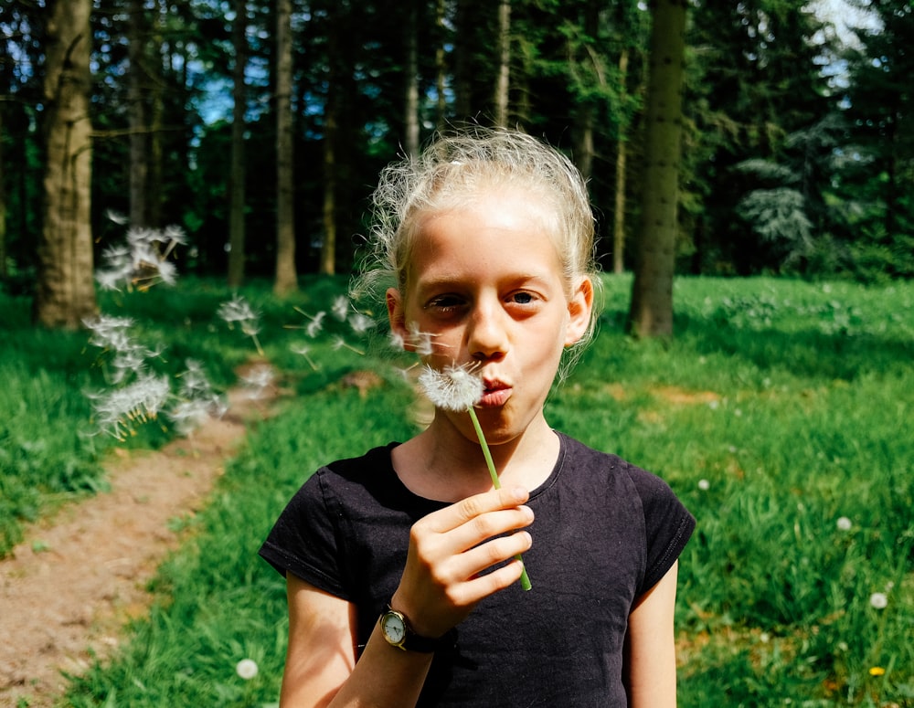 woman in black shirt blowing dandelion