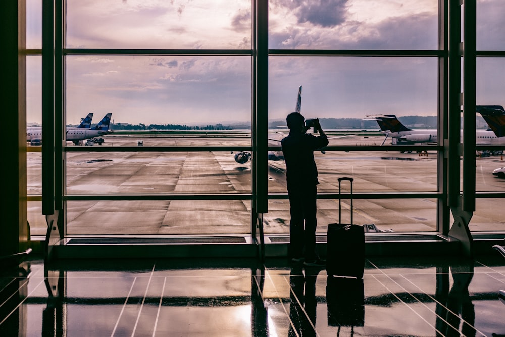 silhueta da pessoa em pé na frente do vidro enquanto tira foto do avião
