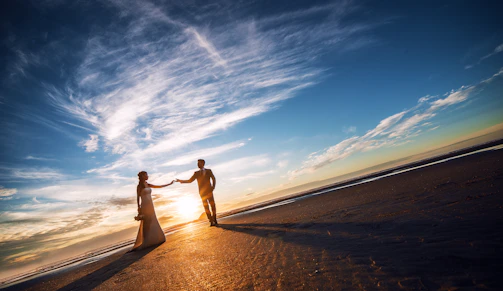 A couple holding hands on a seashore, romantically watching the sunset on a tropical beach.