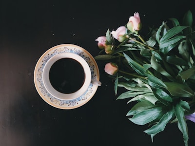 A warm cup of coffee next to a small vase with fresh flowers.