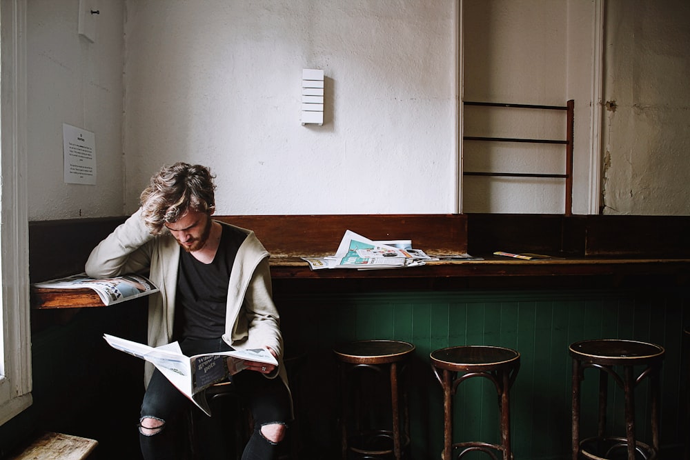 man sitting on bar stool while holding newspaper