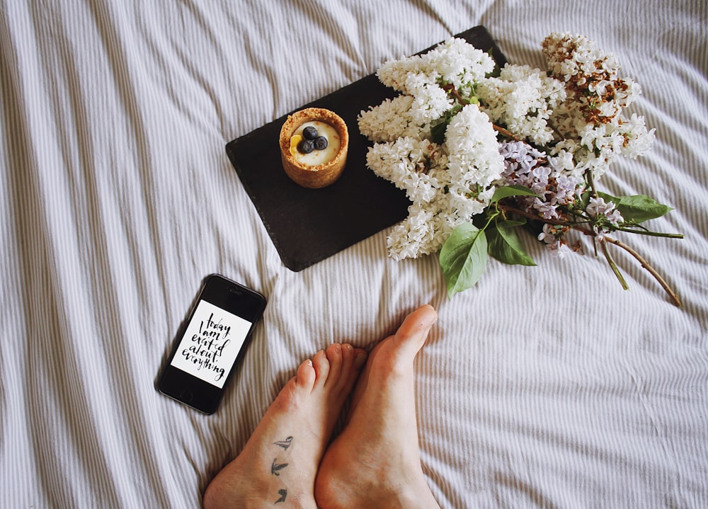 uma pessoa deitada em uma cama com flores e um telefone
