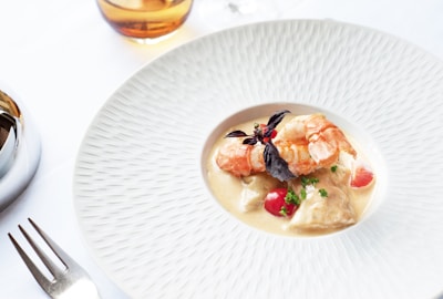 Close-up of a beautifully plated grilled prawn dish with golden accents on a deep navy plate.