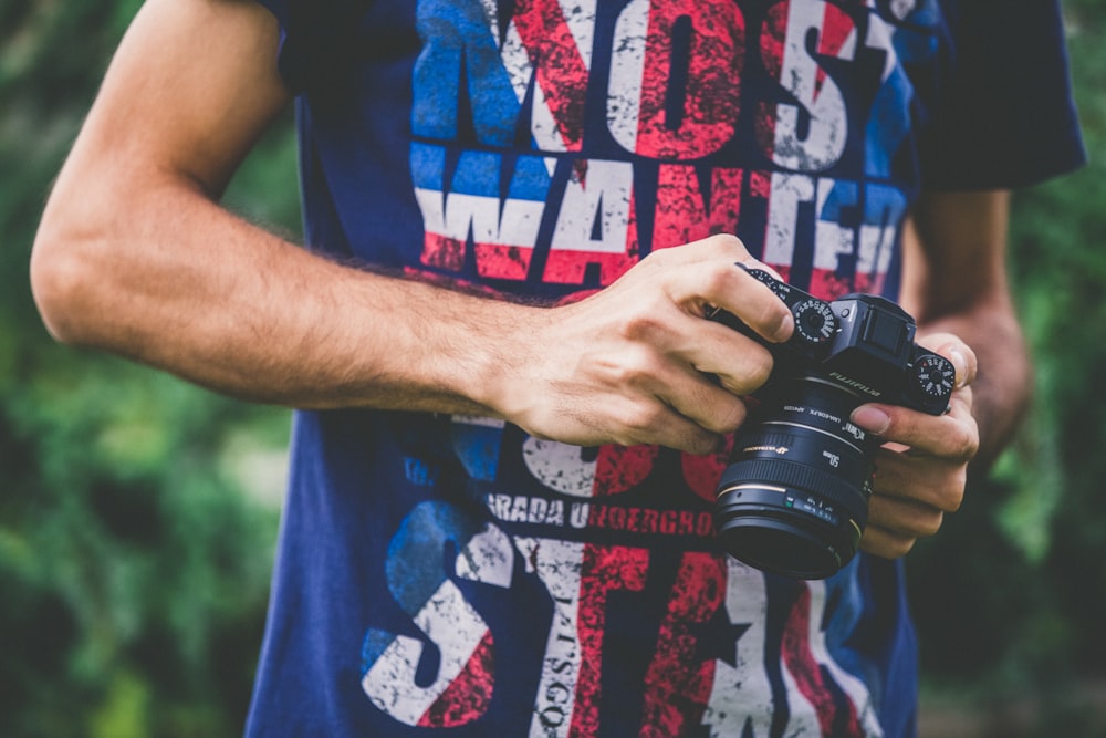 hombre con camisa azul sosteniendo una cámara DSLR