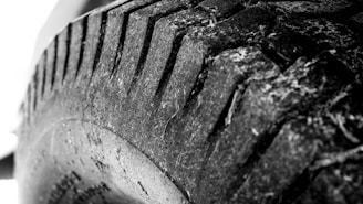 Close-up black and white image of a heavily worn tire tread, showing intricate details of the rubber surface and cracks.