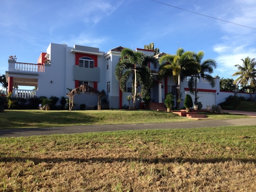 Agent Marlo standing confidently in front of a modern South Florida home with palm trees and clear skies.