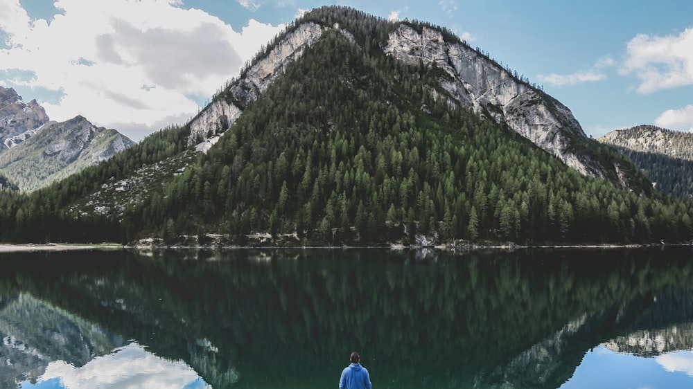 person in blue jacket sitting on blue chair near lake during daytime