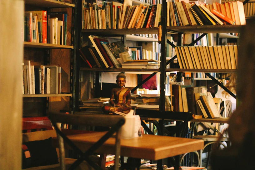 A serene corner with shelves of ancient Vedic scriptures and meditation cushions bathed in warm afternoon light.
