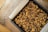 A baking pan filled with a dark, baked dessert topped with abundant pieces of walnuts rests on a cooling rack. The dessert is lined with parchment paper, which extends out of the pan, adding a rustic touch.