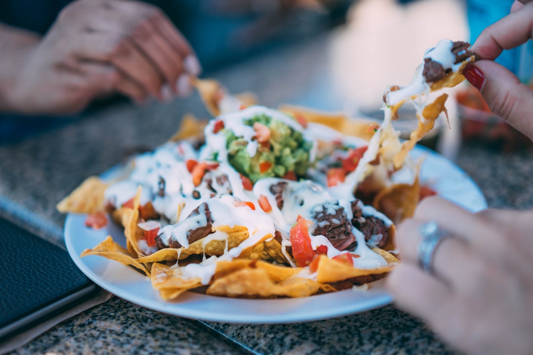 People sharing a plate of Mexican nachos with vegetables and meat