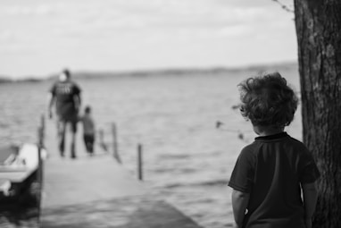 grayscale photography of child beside tree