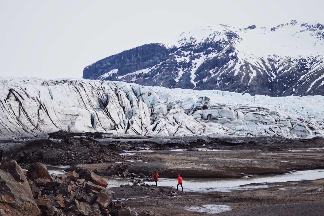 two persons standing near mountain, Following the glacial stream