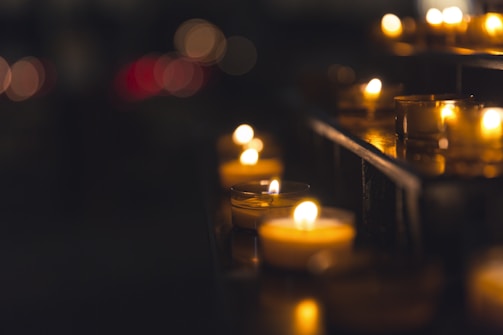 Festive tea light candles arranged in a circular pattern on a cream-colored cloth, glowing softly in a dim room.