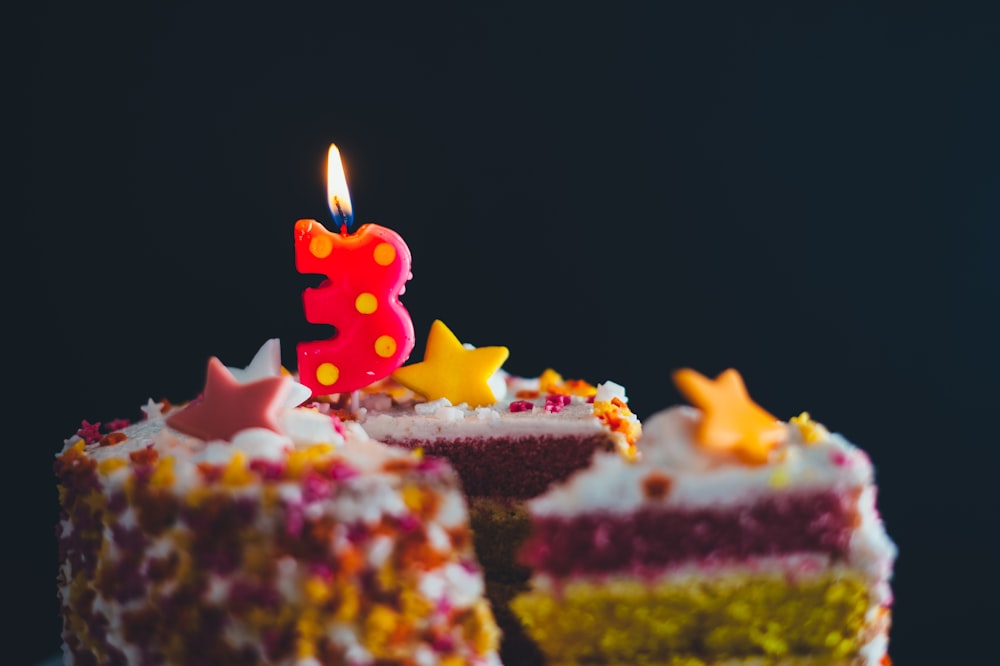 multicolored icing covered cake with 3 cut-out candle