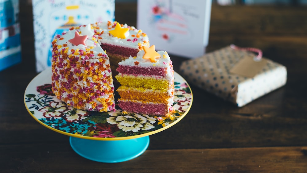 A birthday cake with rainbow sponge and stars on top, with a slice cut out and sat at an angle on the plate