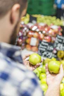 A person in a plaid shirt holding two green apples in a grocery store