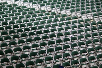 Rows of green chairs are neatly arranged in a spacious area, creating a symmetrical pattern that extends across the image, suggesting a setting prepared for a large audience or event.