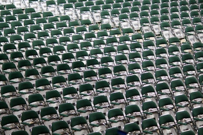 Rows of green chairs are neatly arranged in a spacious area, creating a symmetrical pattern that extends across the image, suggesting a setting prepared for a large audience or event.