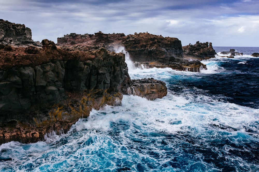 cuerpo de agua chocando contra rocas marrones y acantilado