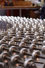 A series of metallic rollers arranged in a repetitive pattern, creating a geometric and industrial look. The focus is on the smooth, cylindrical shapes with a background suggesting a workshop environment.