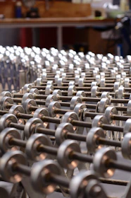 A series of metallic rollers arranged in a repetitive pattern, creating a geometric and industrial look. The focus is on the smooth, cylindrical shapes with a background suggesting a workshop environment.