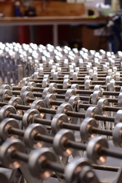 A series of metallic rollers arranged in a repetitive pattern, creating a geometric and industrial look. The focus is on the smooth, cylindrical shapes with a background suggesting a workshop environment.