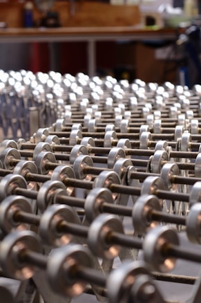 A series of metallic rollers arranged in a repetitive pattern, creating a geometric and industrial look. The focus is on the smooth, cylindrical shapes with a background suggesting a workshop environment.