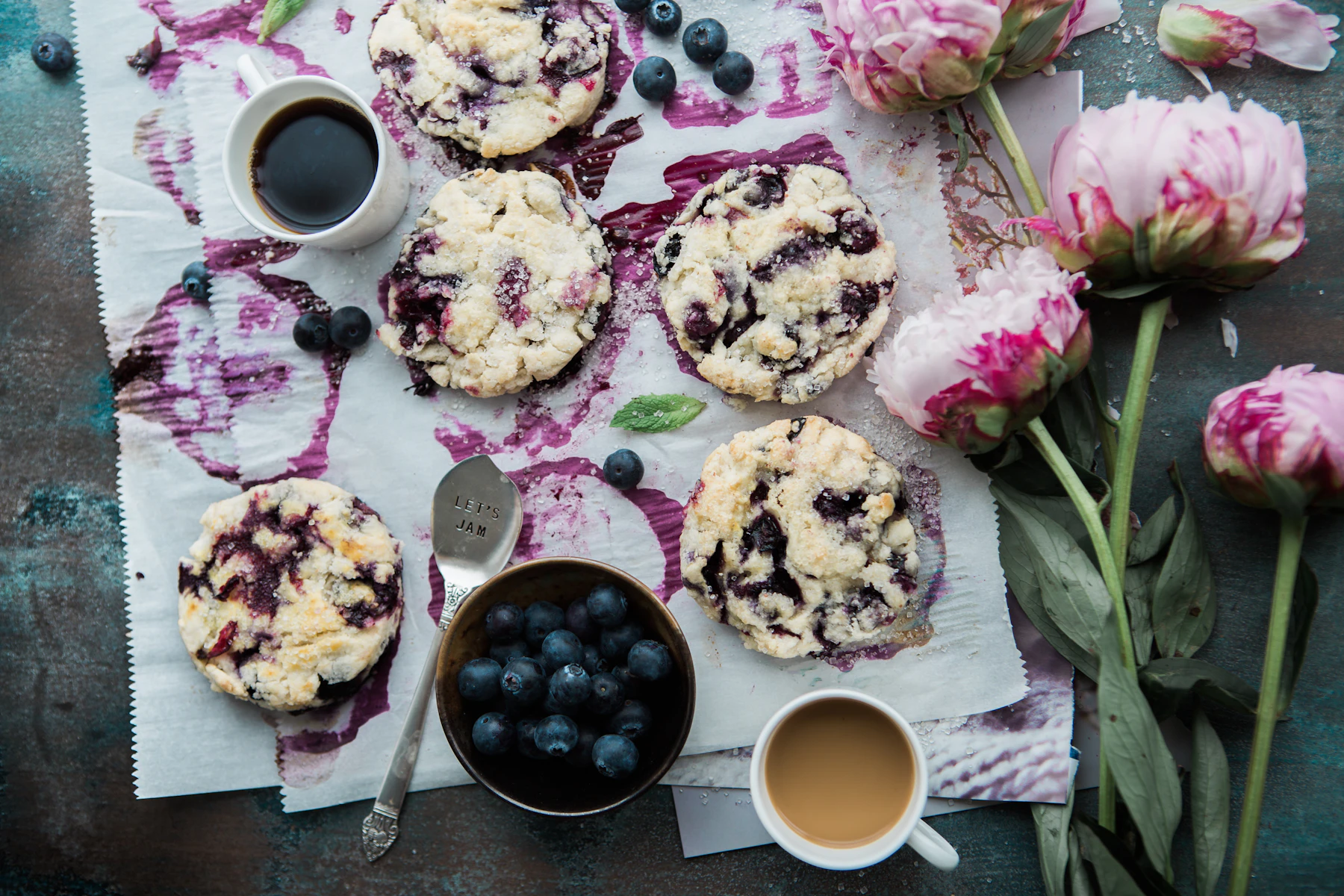 Top-down blueberry scones on a napkin with coffee, fresh blueberries and pink peonies