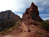 A winding trail leading up to a flat-topped mesa under a cloudy sky.