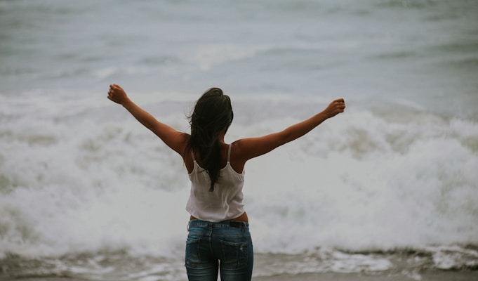 woman in white spaghetti strap top standing on the seashore