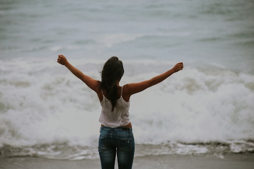 woman in white spaghetti strap top standing on the seashore pain free helped by One Body Acupuncture