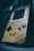 A retro handheld gaming device with a worn, yellowed exterior. The button layout includes a D-pad on the left and two circular buttons on the right, alongside 'Select' and 'Start' buttons. The screen appears slightly damaged with scratches and signs of age.