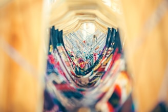 A vibrant and colorful array of hanging clothes seen between wooden hangers, creating a tunnel effect. The focus is on the intricate patterns and vivid colors of the garments, with the background softly blurred.