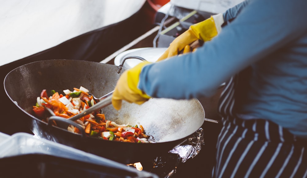 personne mélangeant des légumes dans un wok