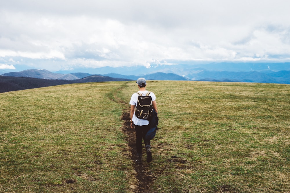 person wearing black backpack walking on green grass field