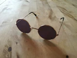 Close-up of aviator sunglasses resting on a sunlit wooden table with soft shadows.