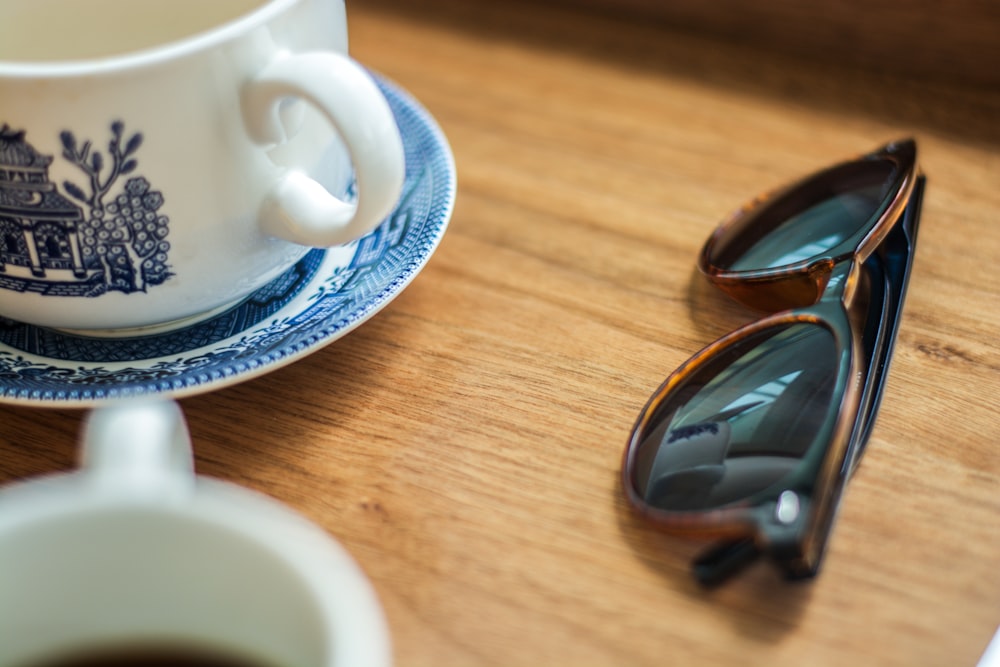 black framed sunglasses beside mug and saucer
