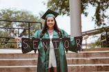 woman wearing green academic dress holding black seniors-printed buntings