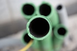 Several cylindrical green pipes are clustered together, shown from the top view with the focal point on the central pipe. The surfaces appear slightly rough, with one pipe showing a chipped edge. The background is blurred, suggesting depth.