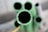 Several cylindrical green pipes are clustered together, shown from the top view with the focal point on the central pipe. The surfaces appear slightly rough, with one pipe showing a chipped edge. The background is blurred, suggesting depth.