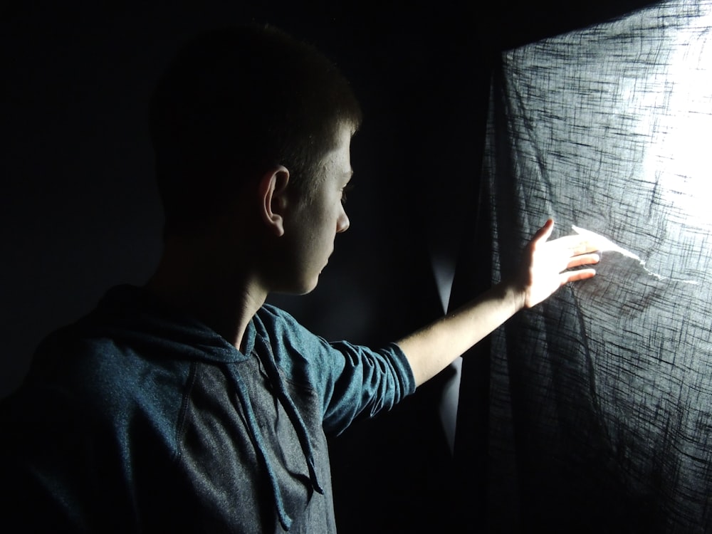 A boy touches the tear of a piece of cloth where light is coming in.